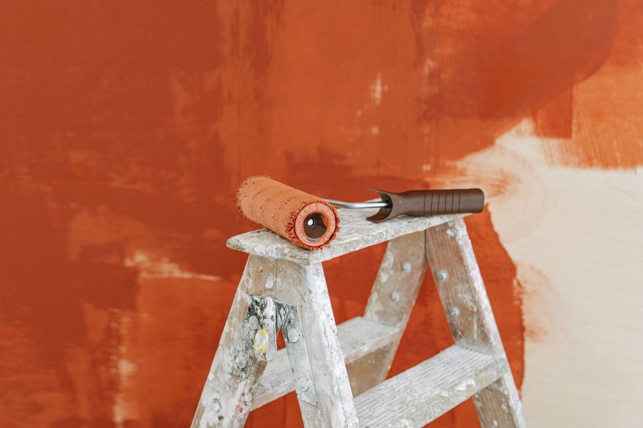 Mastering the First Impression: Your intriguing post title goes here Paint roller on a ladder with a partially painted red wall in the background.