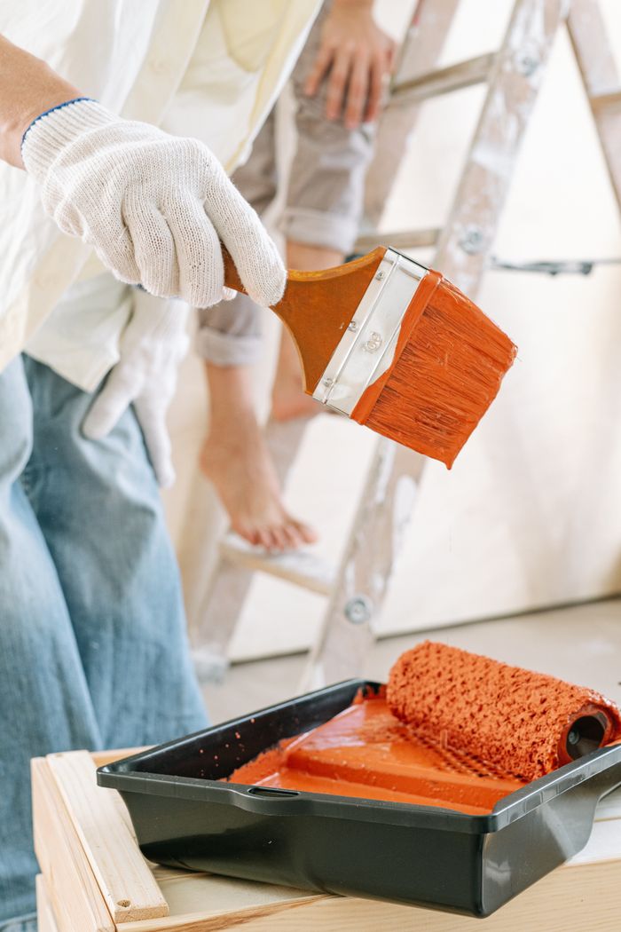Close-up of a person painting walls with red paint, showing tools and detail work.
